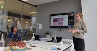 Lunch and learn 380 x 200 A woman stands in a suit jacket giving a presentation in a meeting room