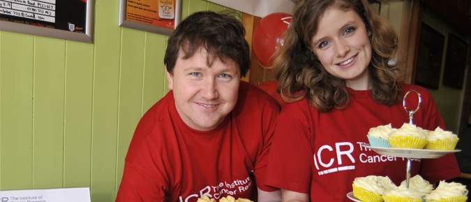 Two fundraisers wearing ICR shirts holding a bake sale
